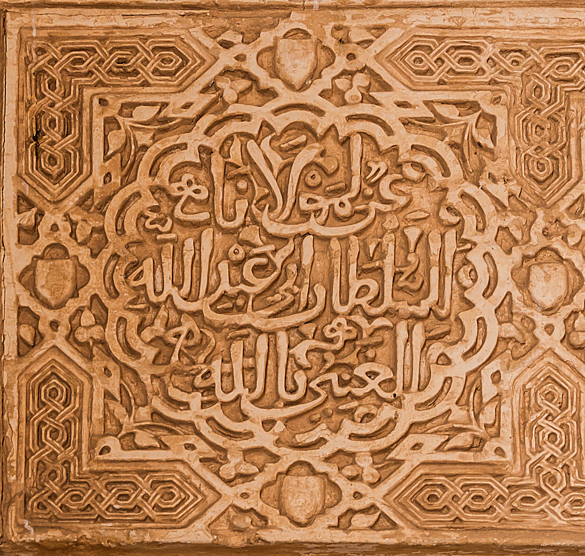 Arabic calligraphy carved in repeating bands across a plaster wall.