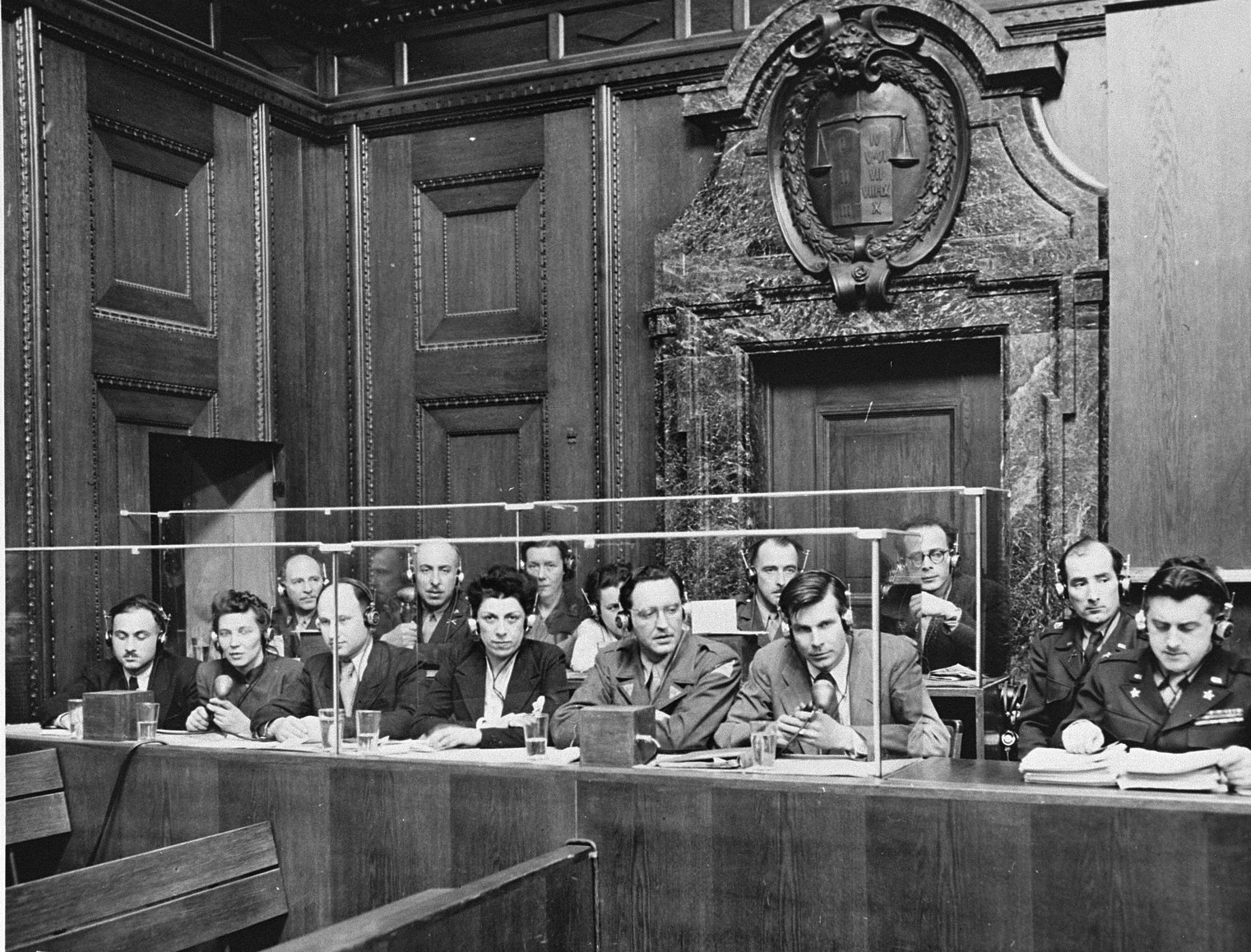 A row of interpreters in headphones seated behind a glass screen in a wood-panelled courtroom, microphones on the desk in front of them.