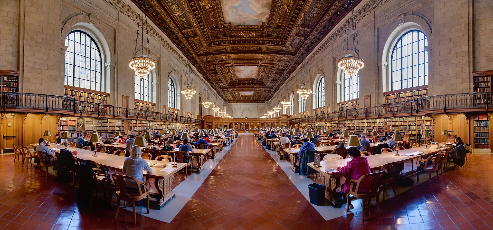 A long library reading room with rows of desks and readers under tall arched windows.