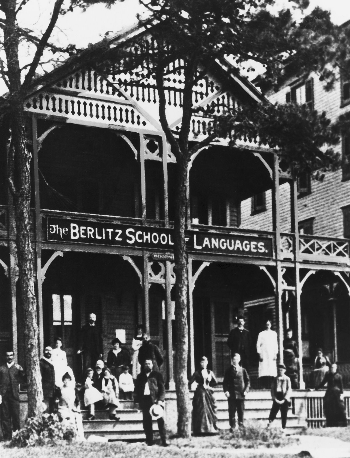 An old photograph of a wooden building with a long painted sign reading The Berlitz School of Languages, people standing on the steps and veranda.