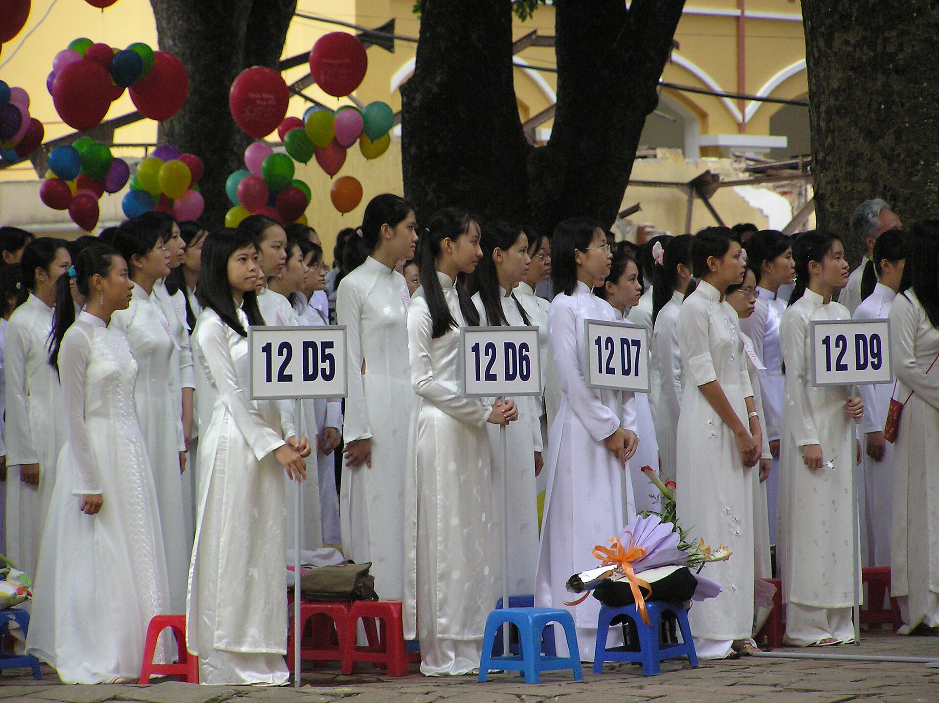 Rows of Vietnamese students in white uniforms standing in a school courtyard at an opening ceremony.