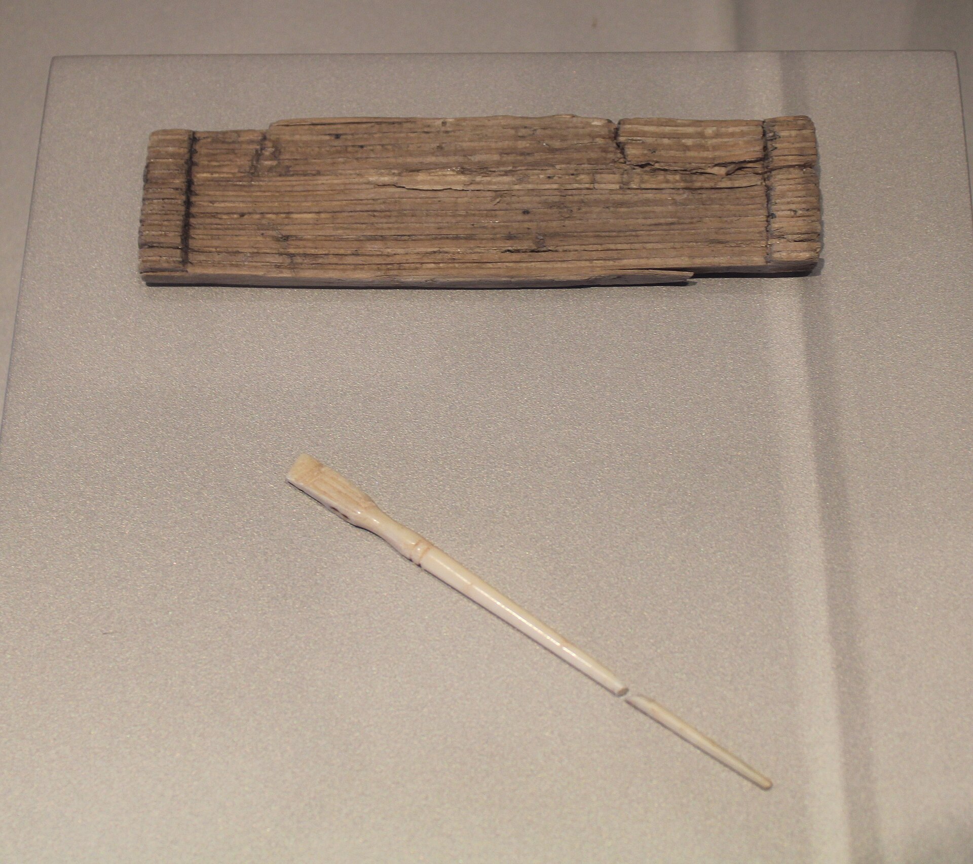 A fragment of a Roman wooden writing tablet displayed above a bone stylus.