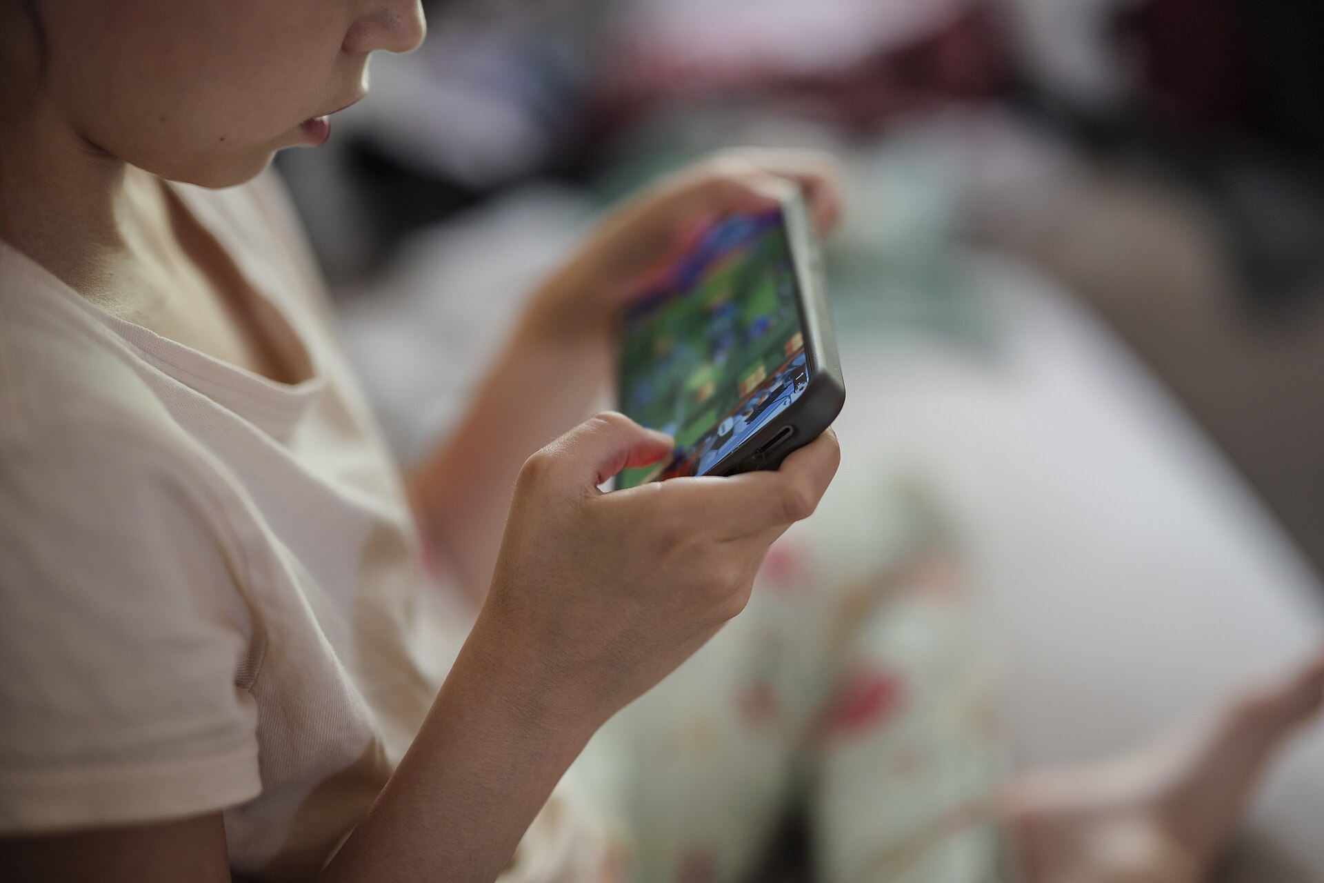 A young child holding a smartphone close, absorbed in the screen.