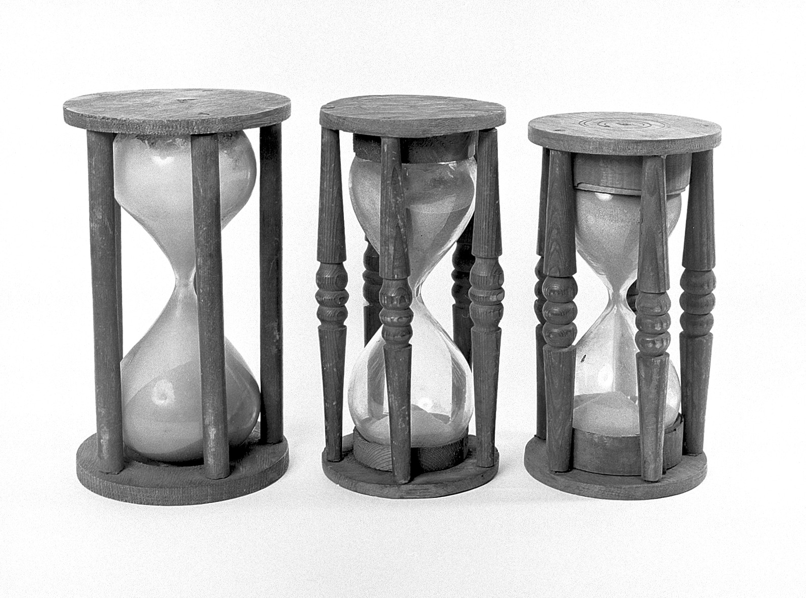 Three hourglasses of different sizes standing side by side, sand part-run in each.