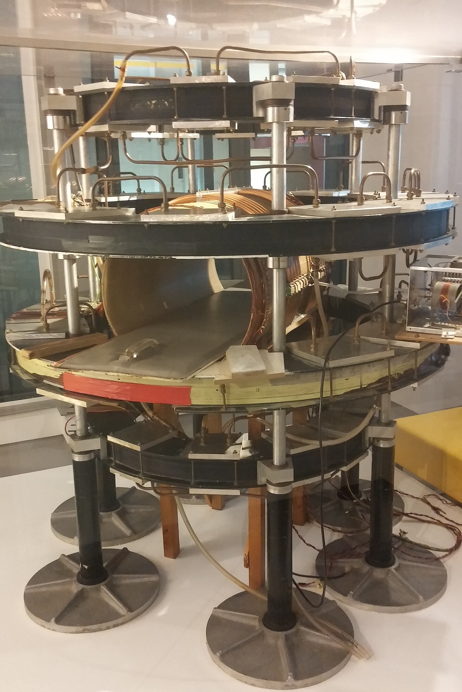 A museum display of an early MRI machine: bare rings of coils on metal stands, wires and copper tubing exposed.