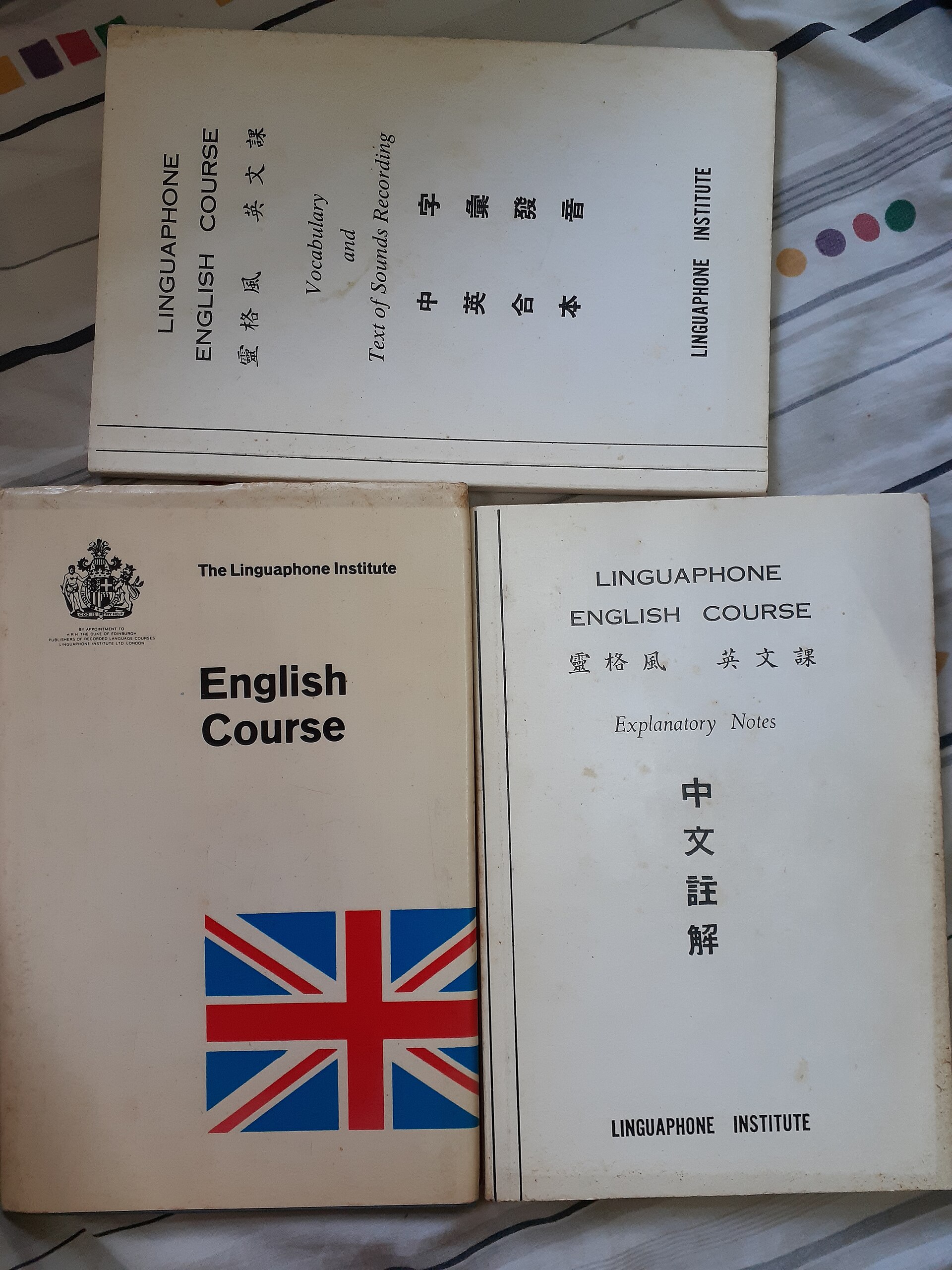 Three volumes of a Linguaphone English Course laid out on a bed, their covers barely worn.