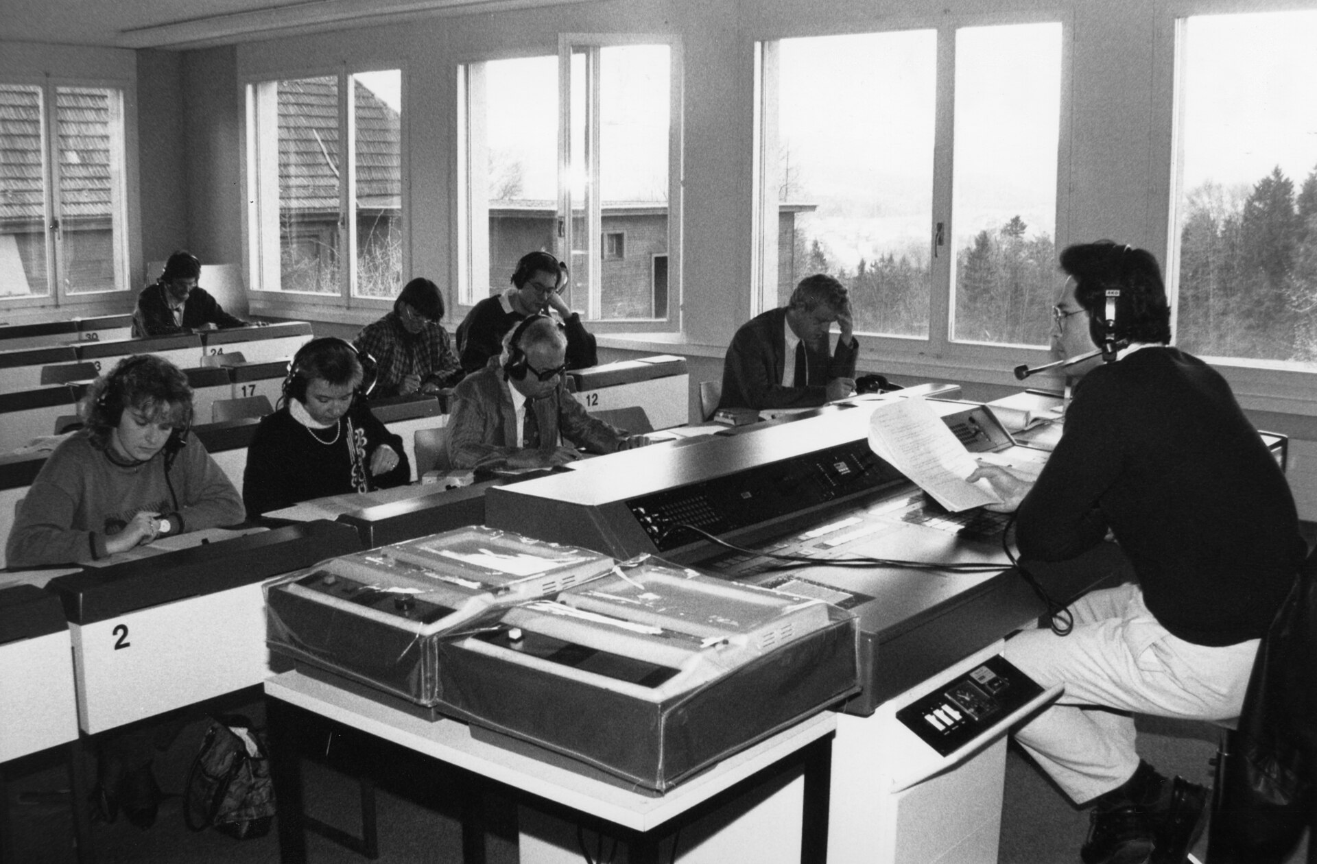 Students in headphones at numbered booths in a language laboratory, an instructor at a console of tape decks.