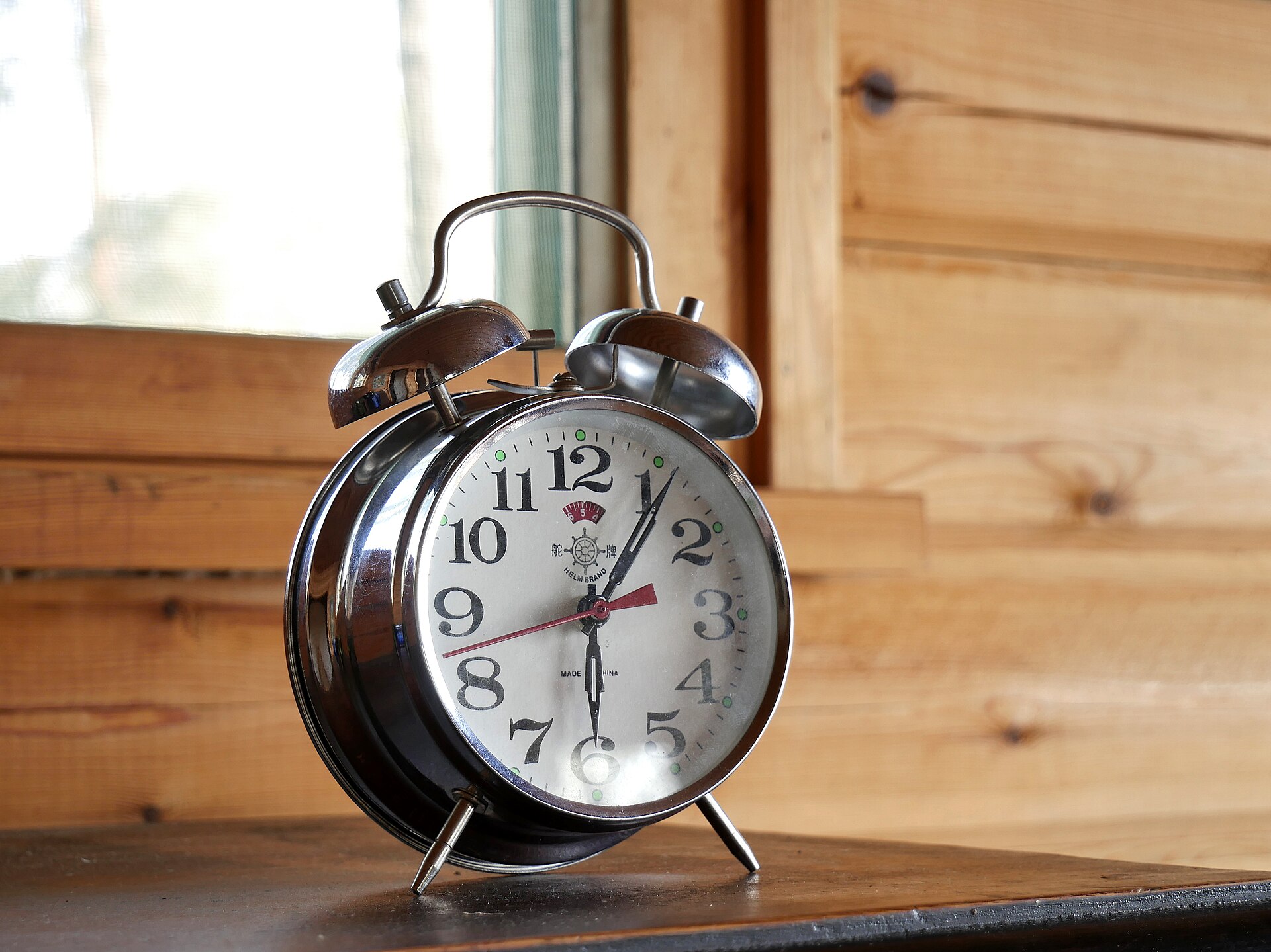 A chrome twin-bell mechanical alarm clock standing on a wooden windowsill.