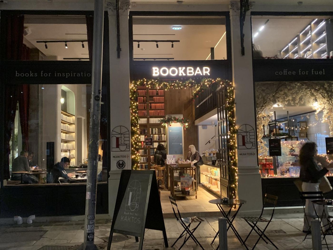 The front of BOOKBAR by Kaktos, a bookshop and café in Athens at night, the windows reading books for inspiration and coffee for fuel