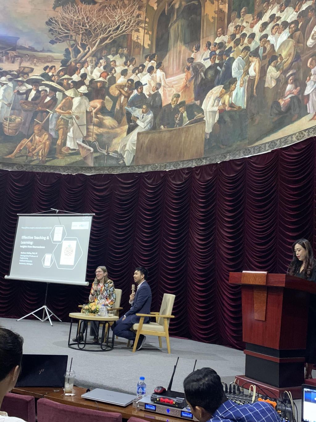 Barbara Oakley in conversation on stage at the Learning How to Learn event in Hanoi, with a slide reading Effective Teaching & Learning: Insights from Neuroscience behind her